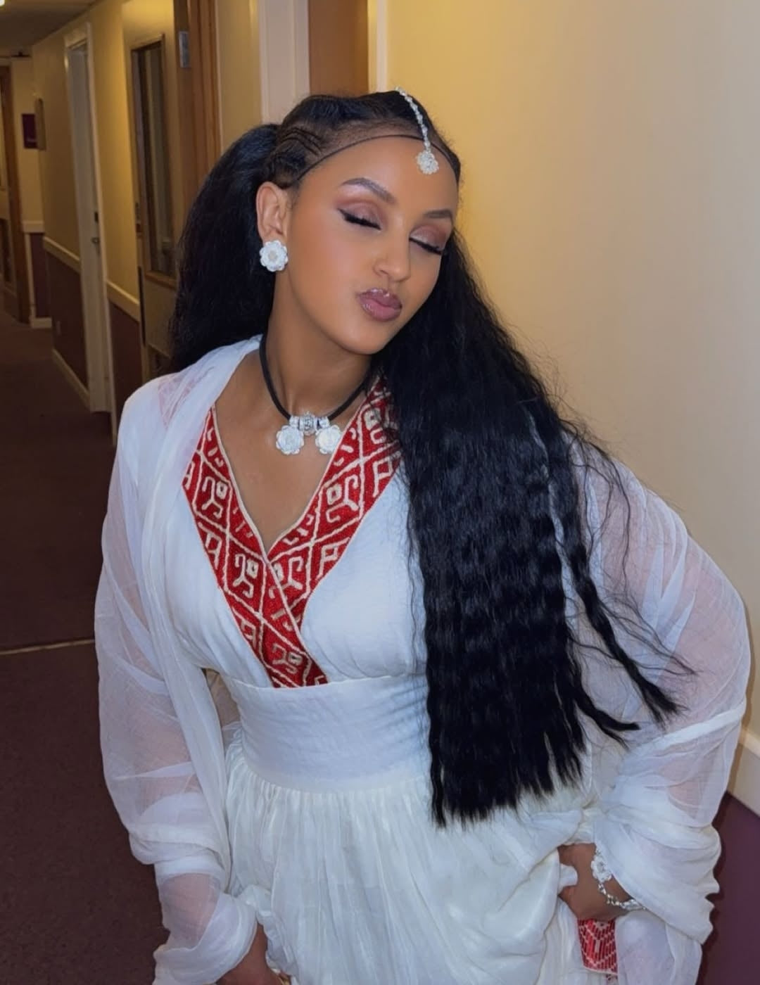 Woman in a white and red habesha kemis with long black hair in a hallway.