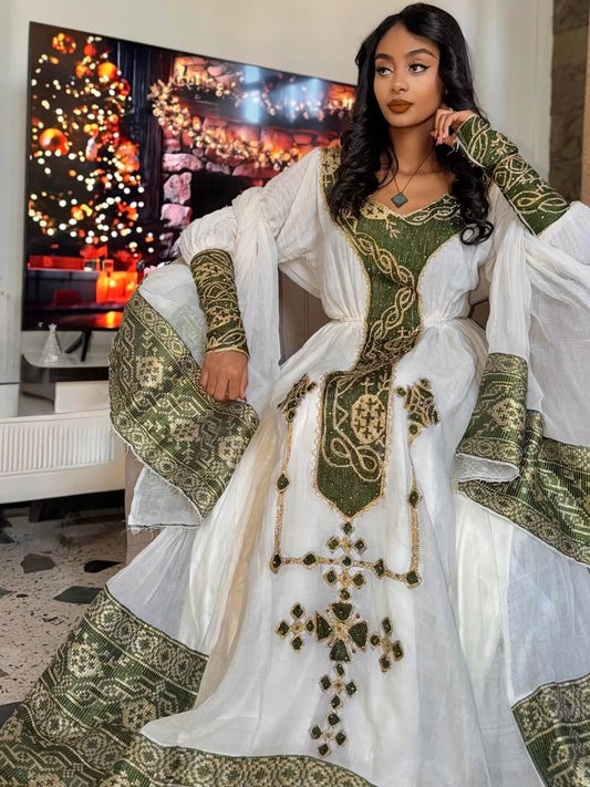 Woman in a white and green embroidered Ethiopian dress sitting in a room with a decorated Christmas tree.