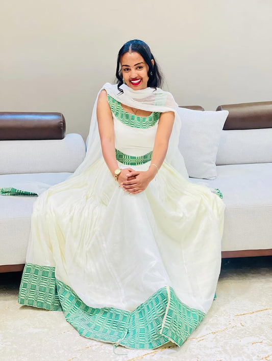 Woman in a white and green Ethiopian cultural dress outfit sitting on a couch.