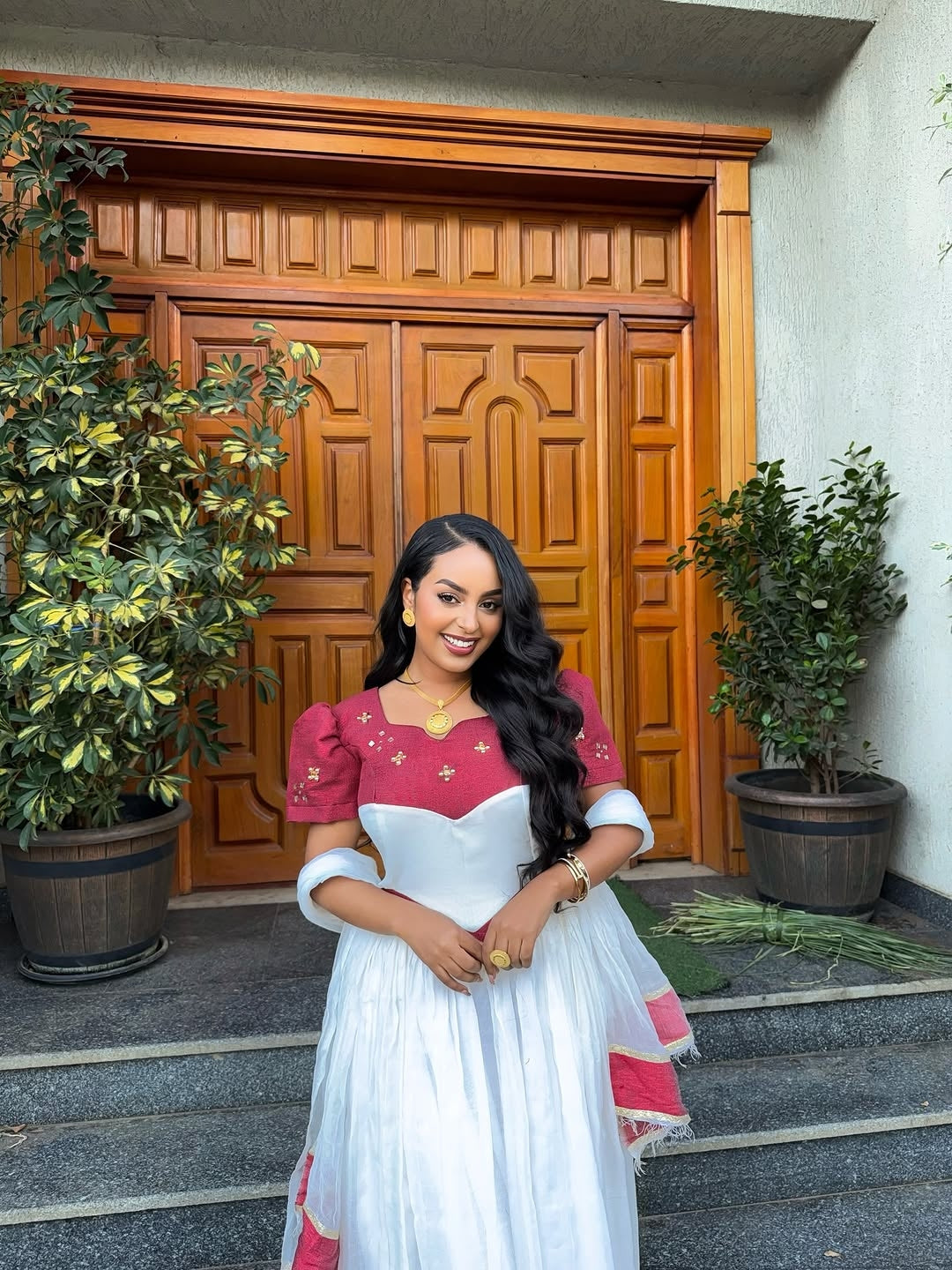 Woman in a white and red traditional Ethiopian cultural dress standing in front of a wooden door.