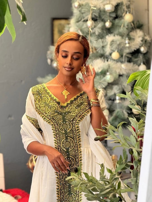 Woman in a green and white traditional Habesha Zuria standing in front of a decorated Christmas tree.