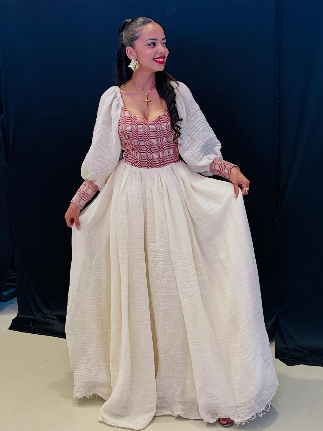 Woman in a traditional Habasha dress with a white top and long white skirt against a dark background