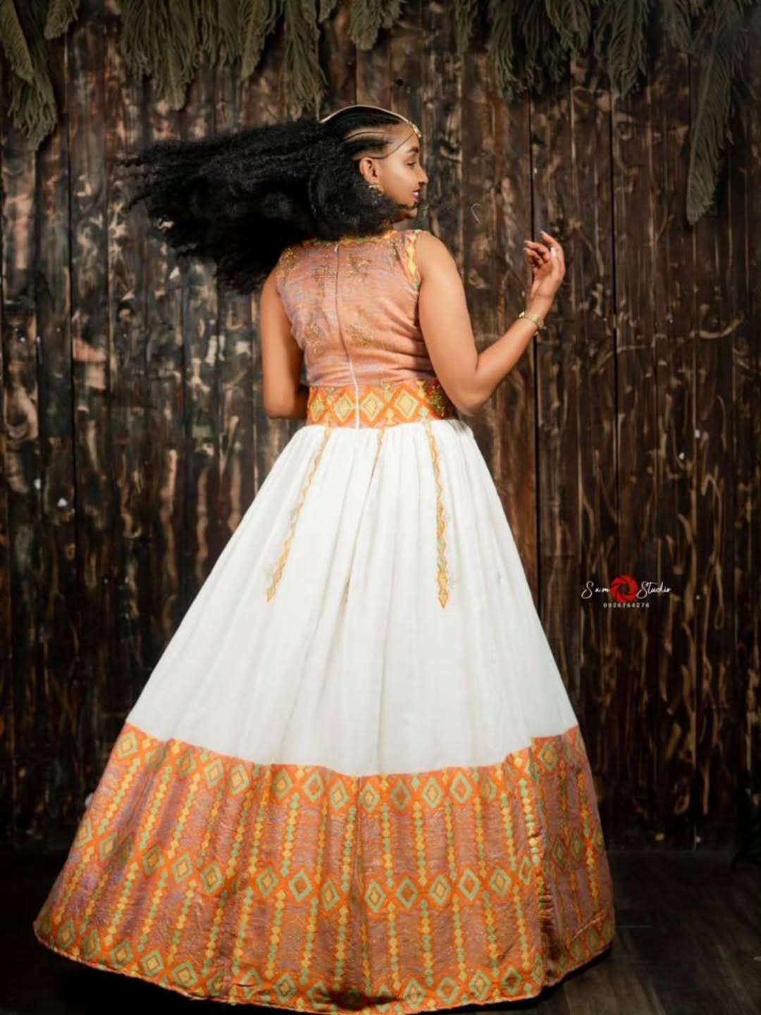 Woman wearing a traditional habesha kemis with a white and orange patterned dress against a wooden background