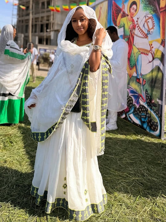 Woman in Ethiopian Traditional Dress with green accents standing outdoors with a colorful mural in the background.