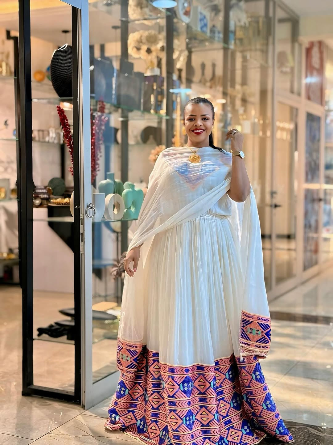 Woman in a white and patterned Habesha Dress standing in a store.