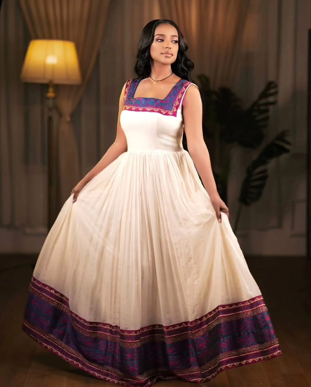 Woman wearing a white Ethiopian Dress with colorful accents in a room setting