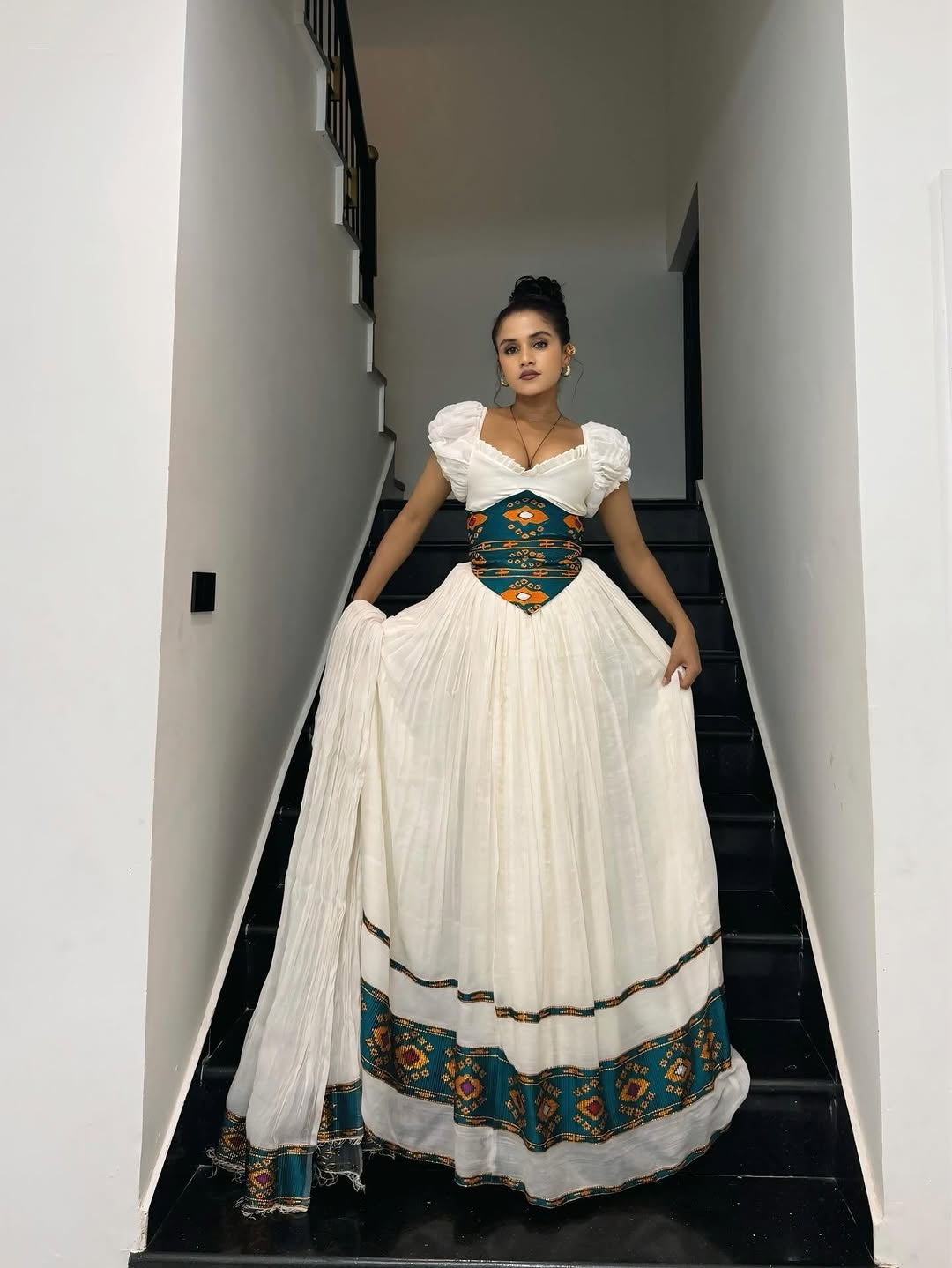 Woman in a traditional Ethiopian cultural dress with white dress and blue accents walking down a staircase.