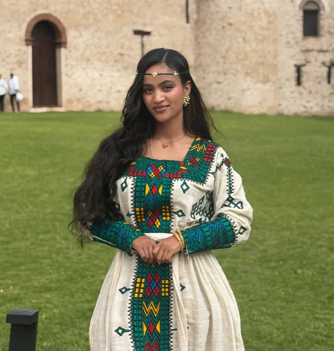 Woman in Ethiopian Traditional Dress embroidered dress standing in front of a stone building