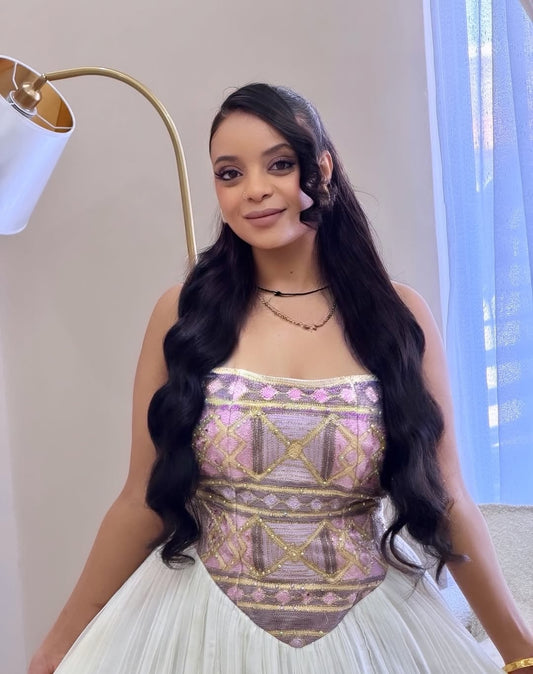 Woman wearing a patterned top and white Ethiopian dress indoors