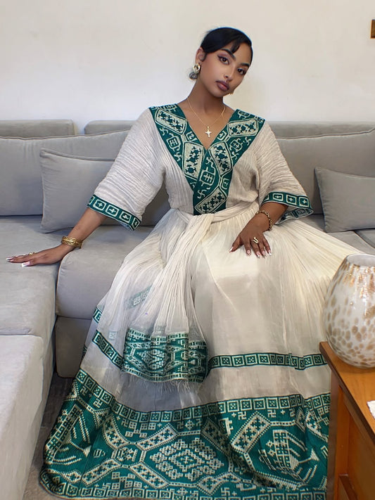 Woman in a traditional outfit with green and white Ethiopian cultural dress sitting on a couch.