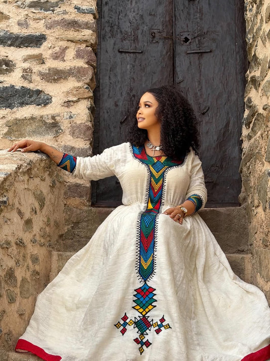 Woman in a Ethiopian Libs with colorful embroidery sitting against a stone wall.