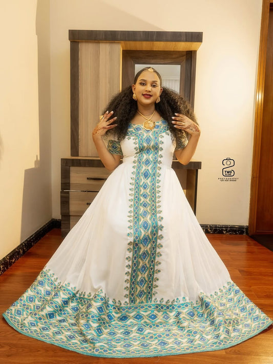 Woman wearing a Green Habesha Zuria with blue embroidery in a room.