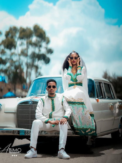 Two people in formal attire sitting on a vintage car with a scenic background