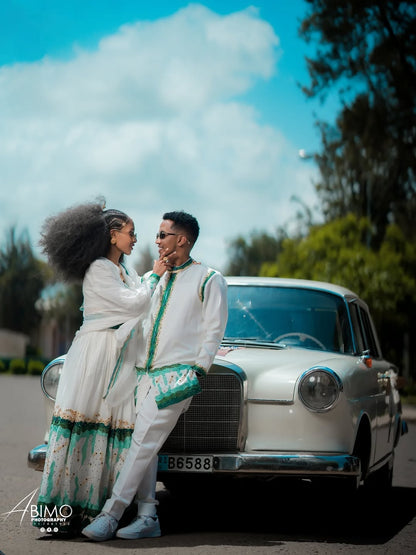Couple in formal attire standing next to a vintage car with a scenic background