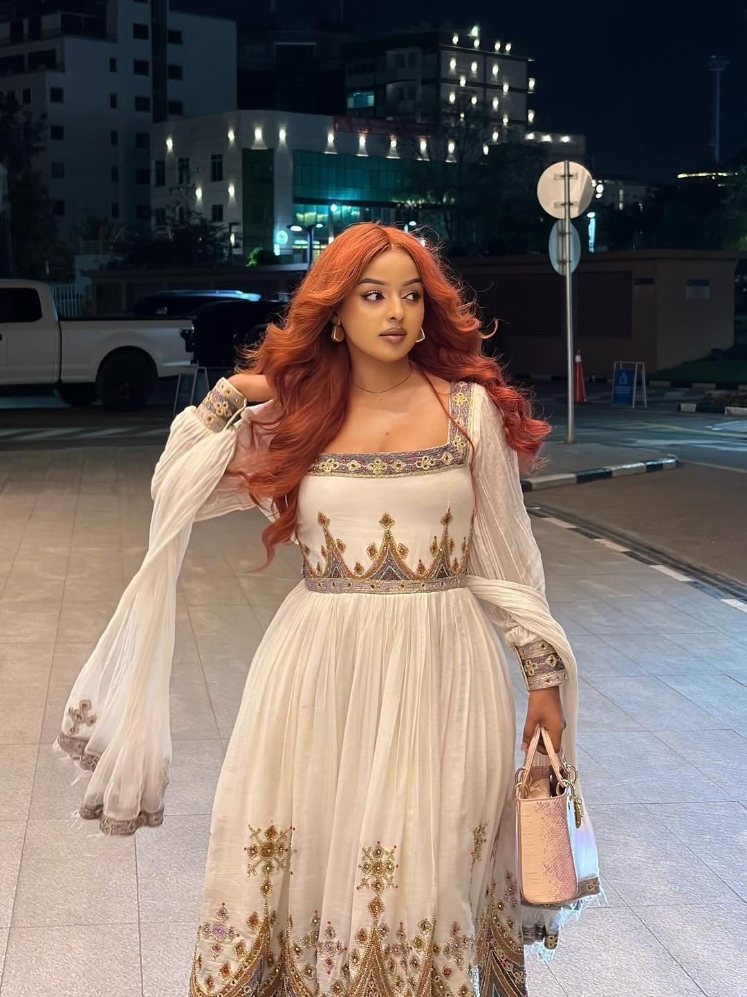 Woman in an Gold Habesha Zuria dress standing on a street at night.
