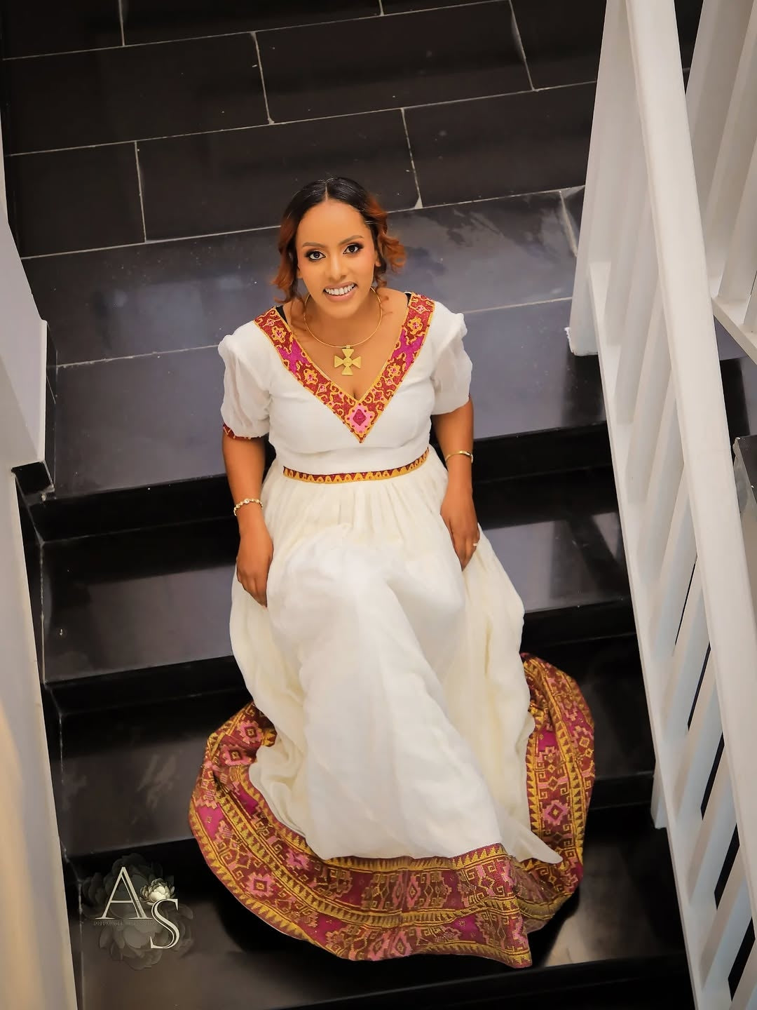 Woman in a white and red traditional habesha dress sitting on a staircase.