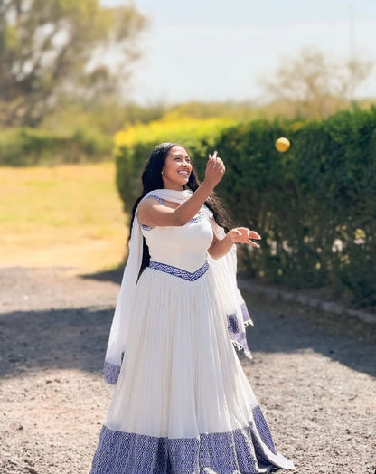 Woman in a Blue Habesha Zuria with blue accents playing with a yellow ball outdoors.