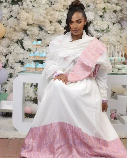 Woman in a white and pink Ethiopian cultural dress sitting in front of floral decorations.