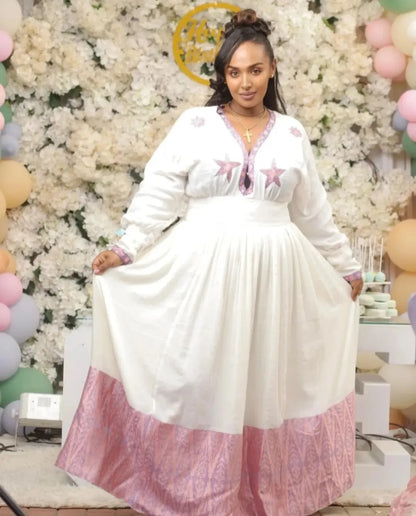 Woman in a Ethiopian cultural dress with pink accents standing in front of a decorated wall with balloons.