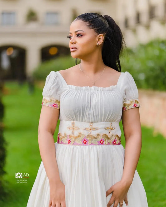 Woman in a white Pink Habesha Zuria with floral embroidery standing outdoors.