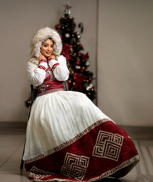 Woman wearing a white Ethiopian cultural dress with red patterned hem against a plain background