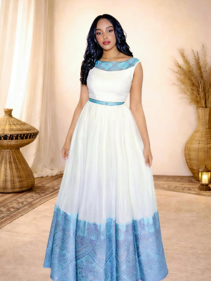 Woman wearing a white Habesha Dress with blue accents in a decorated room.
