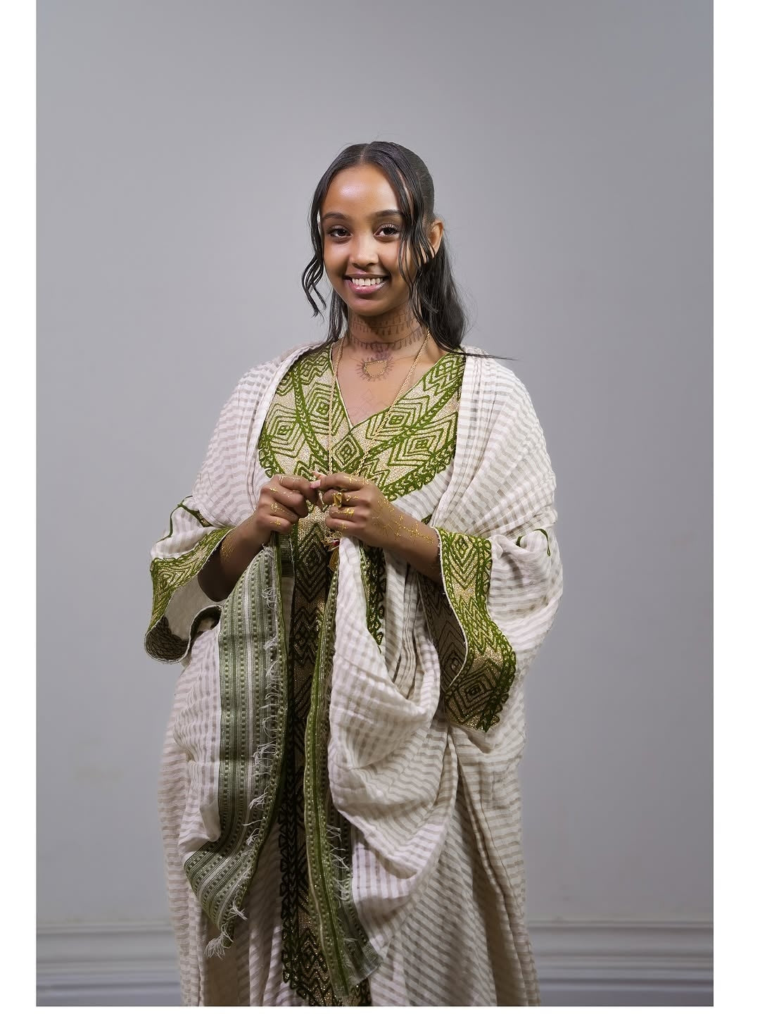 Woman wearing Ethiopia traditional dress a white and green patterned against a gray background