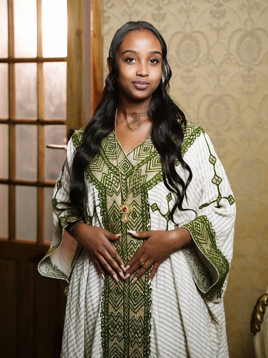 Woman wearing Ethiopia traditional dress a green and white patterned  against a decorative wall.