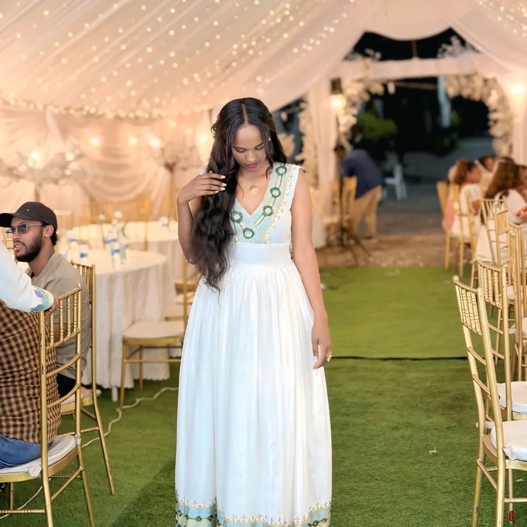 Woman in a white Ethiopian cultural dress standing in an outdoor event setting with tables and chairs.