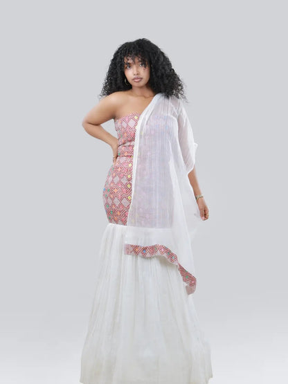 A woman modeling a white dupatta draped over a pink and white patterned strapless Habesha Kemis against a solid light gray background.