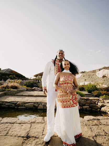 Two people standing outdoors in traditional attire with a scenic background