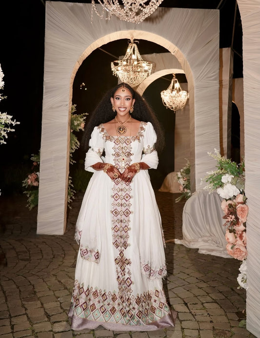 Woman in a white embroidered dress standing in front of an archway with chandeliers and floral decorations.