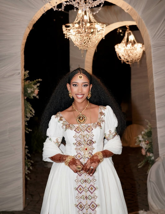 Woman in a white embroidered dress standing in front of a decorative arch with chandeliers.