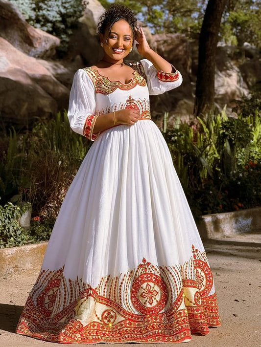 Woman in a white Ethiopian cultural dress   with red and gold embroidery standing outdoors.