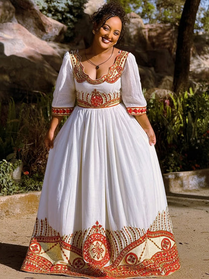 Woman wearing a white Ethiopian cultural dress   with red and gold patterns outdoors.