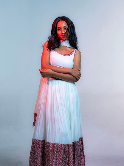 Woman wearing a long, patterned Ethiopian cultural dress with a plain background