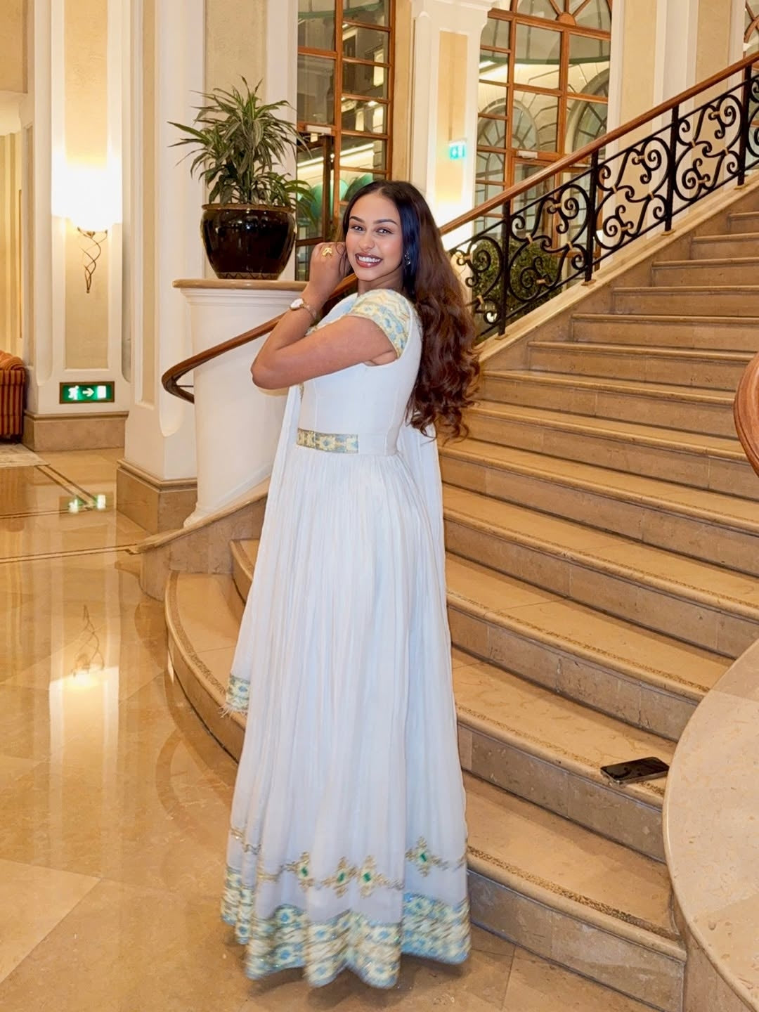 Woman in a white Ethiopian dress  saree standing on a staircase in an elegant interior setting