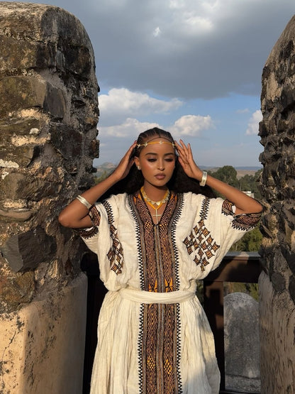 Woman in a traditional Gonder fetel standing between stone walls with a scenic background