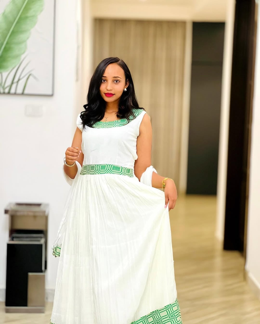 Woman in a white dress with green accents standing in an indoor setting.