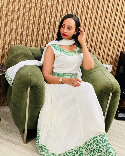 Woman in a white and green traditional outfit sitting on a green chair.