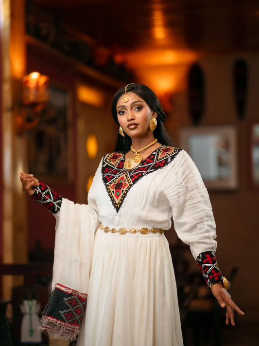 Woman in a traditional outfit with intricate patterns in a warm-toned room.