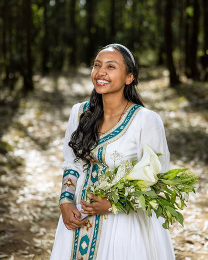 Woman in a white Green Habesha Wedding Couple Outfit with green patterns holding flowers in a forest setting