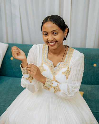 Woman in a white dress with gold embroidery sitting on a teal couch.