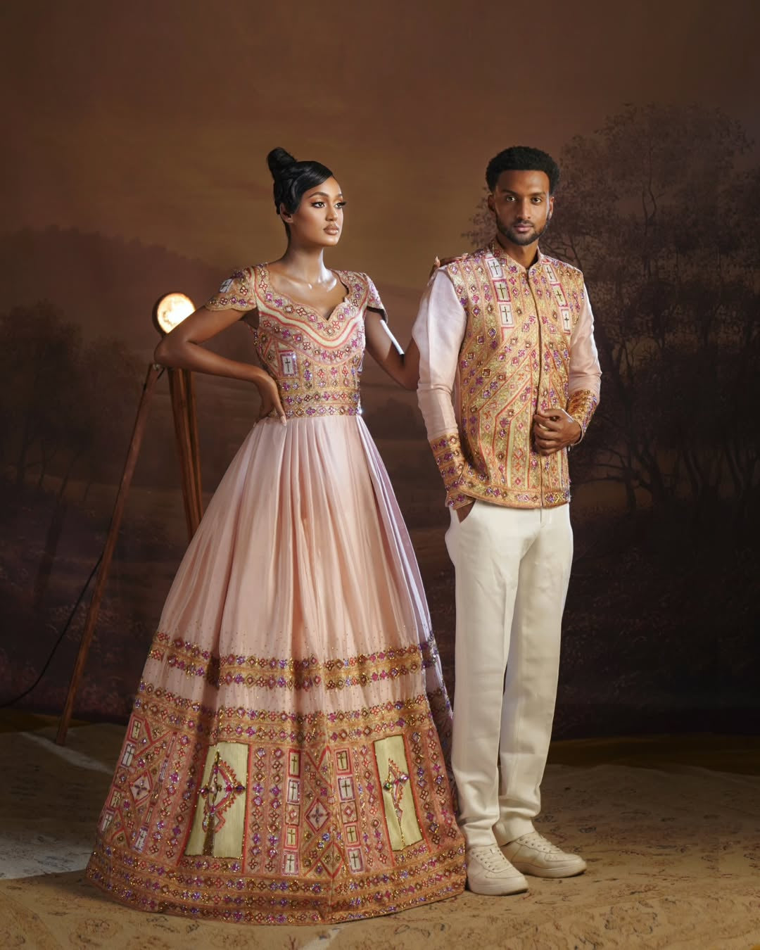 Man and woman in traditional Habesha Outfit couple Set  standing against a textured brown background