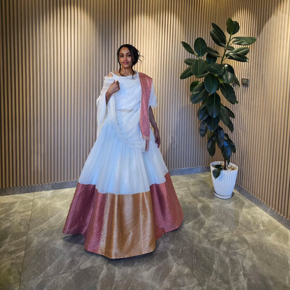 Woman in a white and red traditional habesha kemis  standing indoors next to a plant.