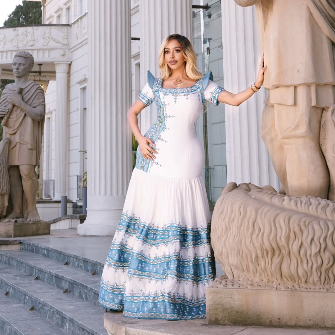 Woman in a white and blue habesha kemis standing in front of classical statues.
