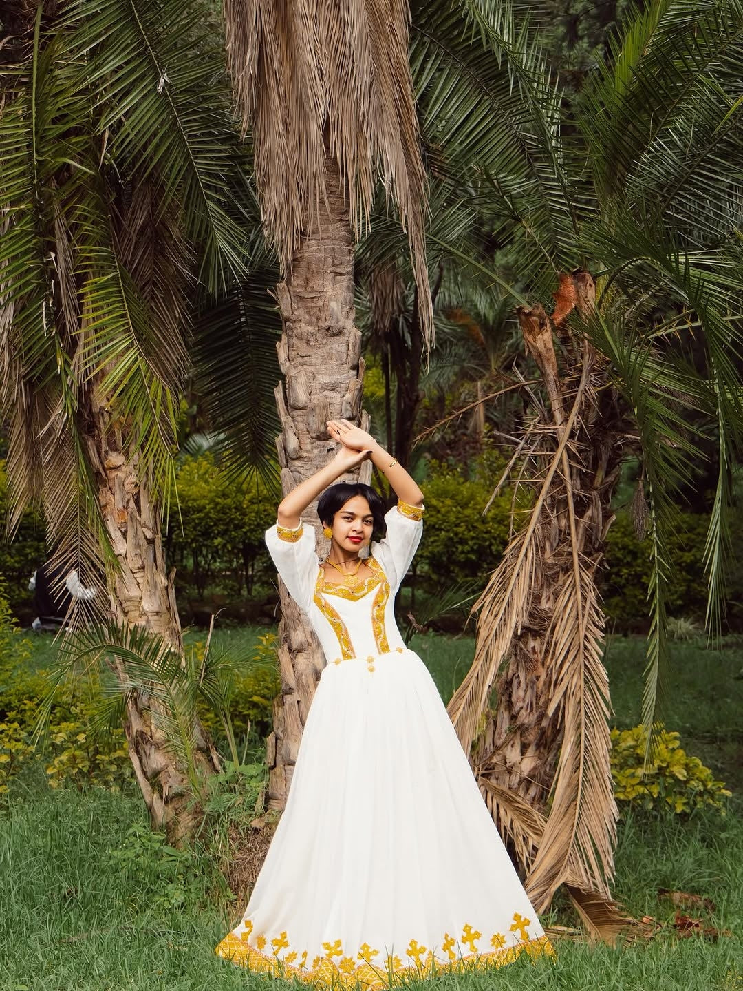 Woman in a white and yellow dress standing in a garden with palm trees.
