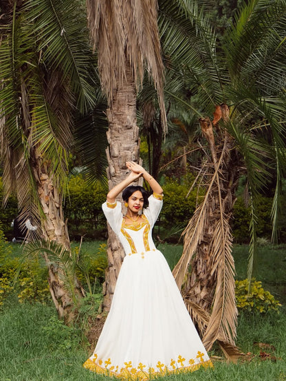 Woman in a white and yellow dress standing in a garden with palm trees.