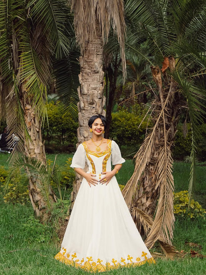 Woman in a white and yellow dress standing in a garden with palm trees.