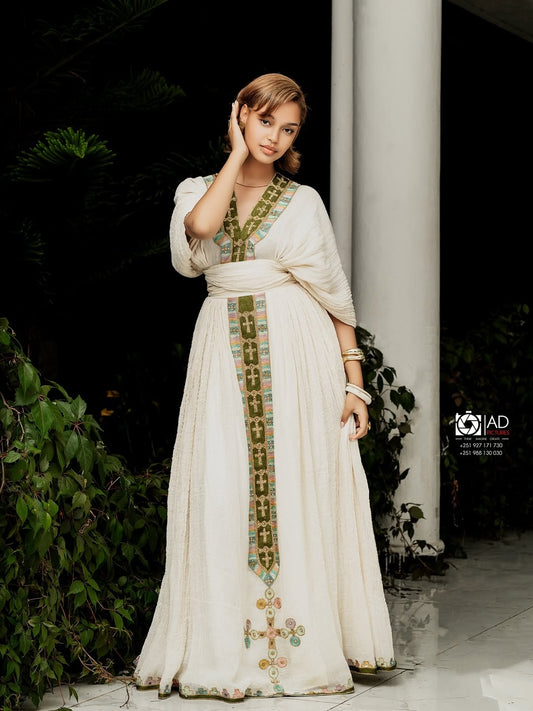 Woman in a white Ethiopian cultural dress with green embroidery standing outdoors.